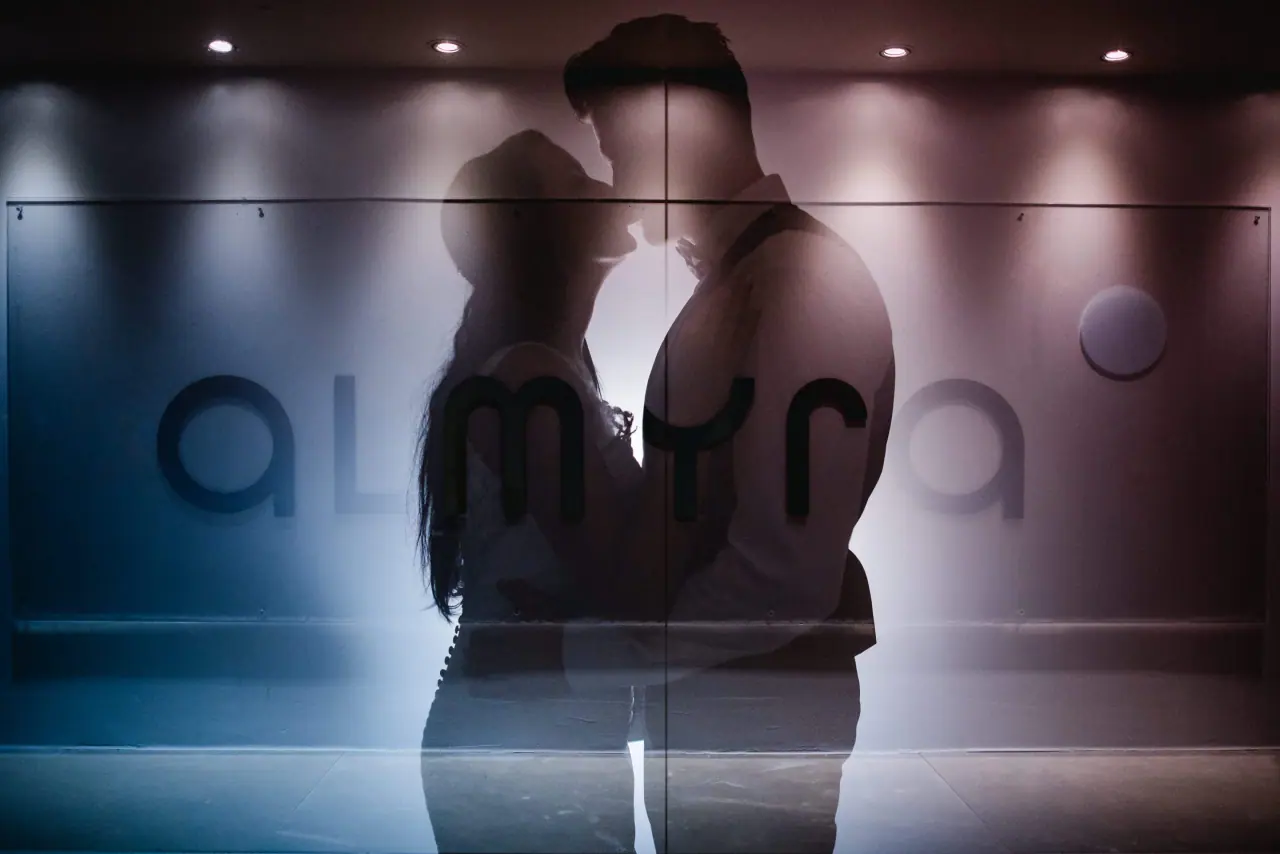 Silhouette of Jaclyn and Steven about to kiss before the illuminated Almyra sign, Paphos