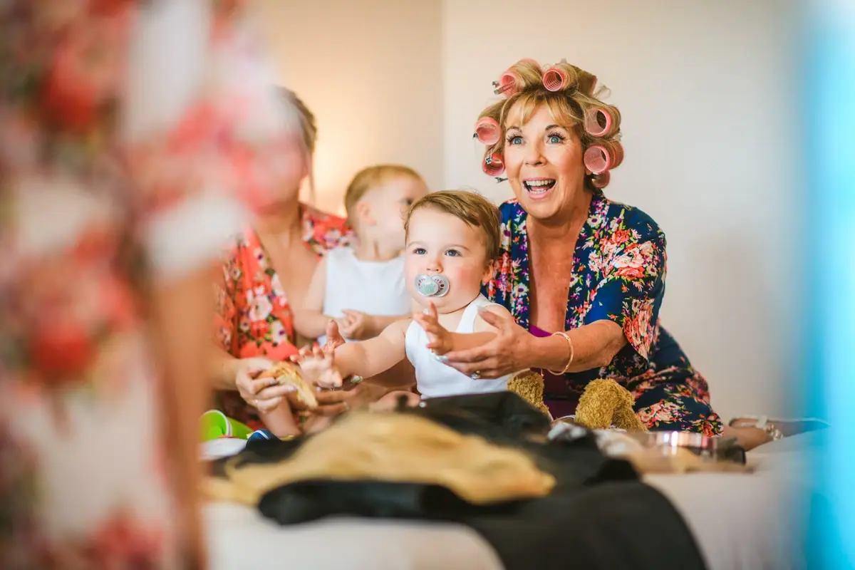 Woman in hair rollers laughing with a baby during bridal preparations