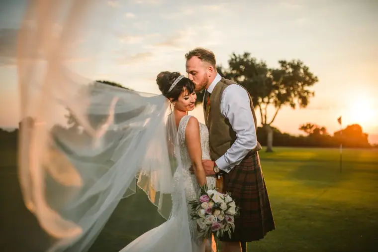 Melissa's veil blowing in the wind as Marc kisses her forehead at sunset, Aphrodite Hills