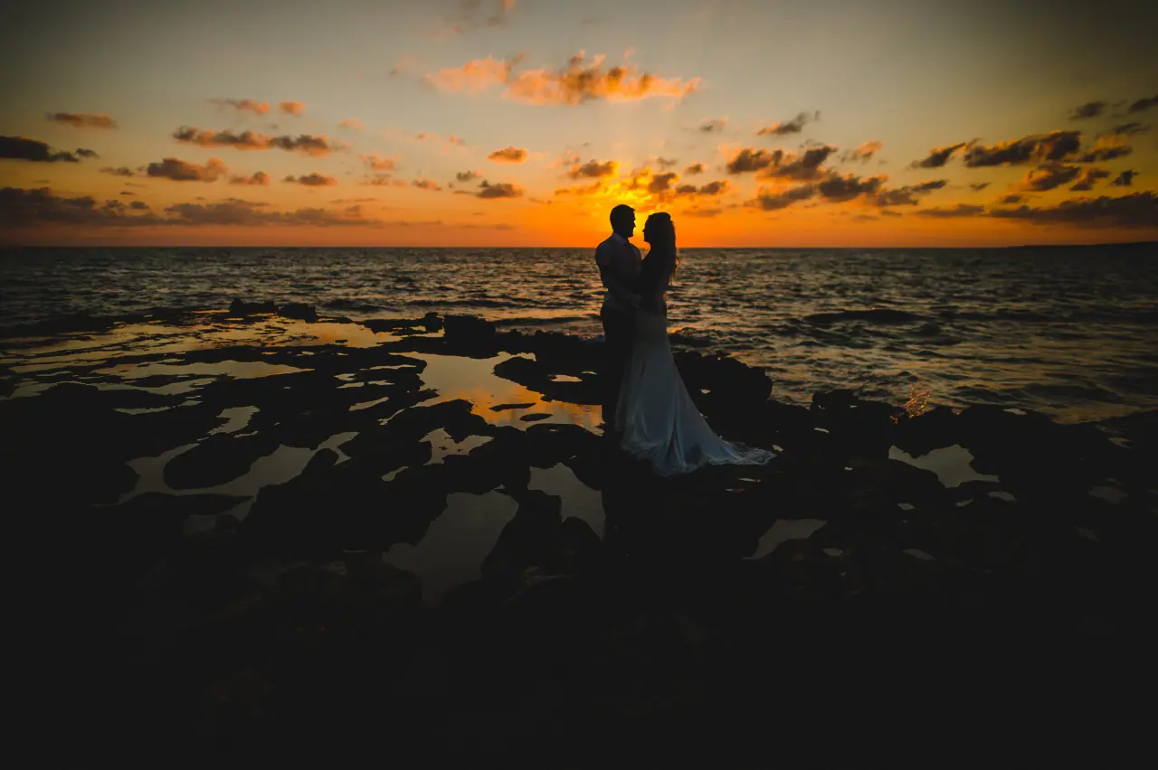 Lisa and Adam silhouetted against a fiery sunset on the rocky Paphos coast