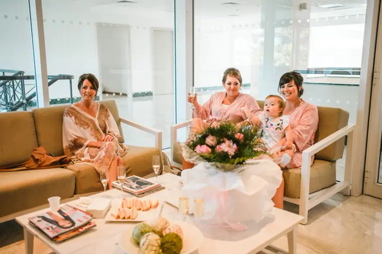 Bridal party relaxing in pink robes on sofas around a bouquet in a bright lounge