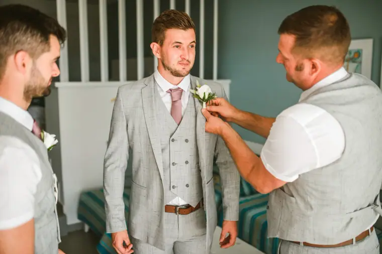 Groomsman pinning a buttonhole on the groom's grey suit