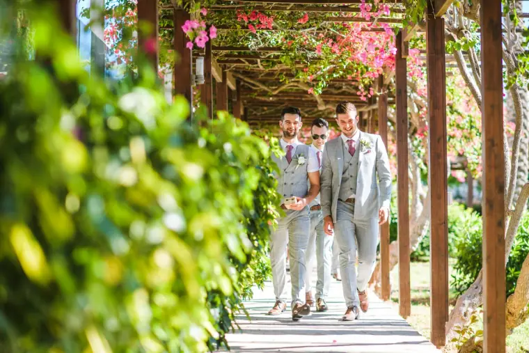 Groom and groomsmen walking under a bougainvillea-covered pergola