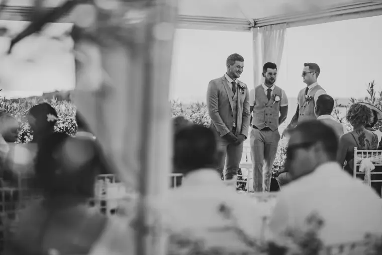 Black-and-white shot of the groom and groomsmen waiting under the canopy