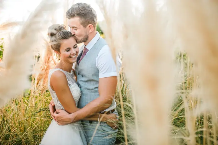 Groom kissing his bride's forehead among feathery pampas grass