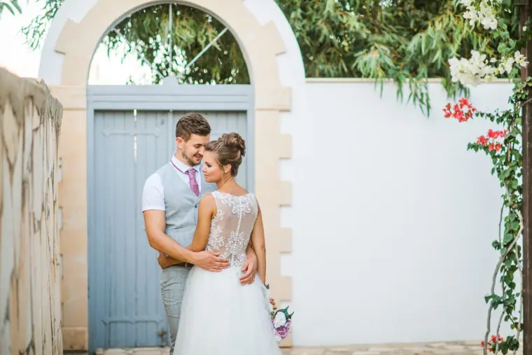 Couple embracing in front of a blue arched gate in a white wall