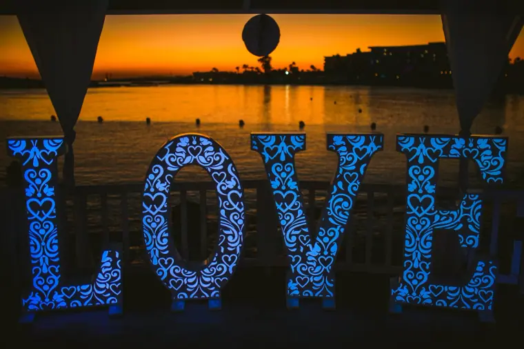 Light-up LOVE letters glowing blue against an orange sunset over the sea