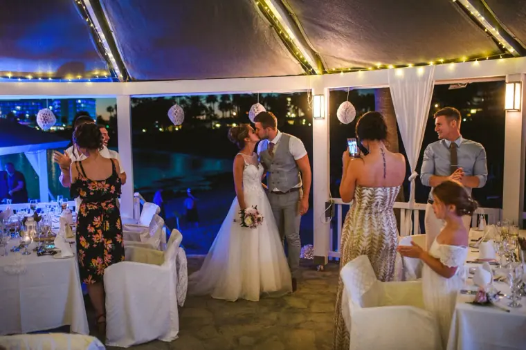 Bride and groom kissing in the reception marquee as guests take photos