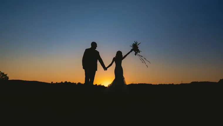 Emily and Chris silhouetted at dusk with the bouquet raised at Minthis, Paphos