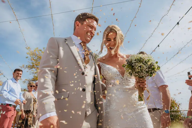 Bride and groom laughing as guests throw confetti at Liopetro