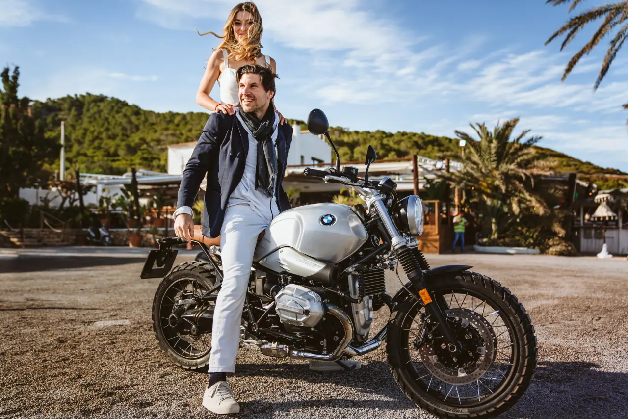 Birger on a motorbike as Antonia stands on the back, arms raised