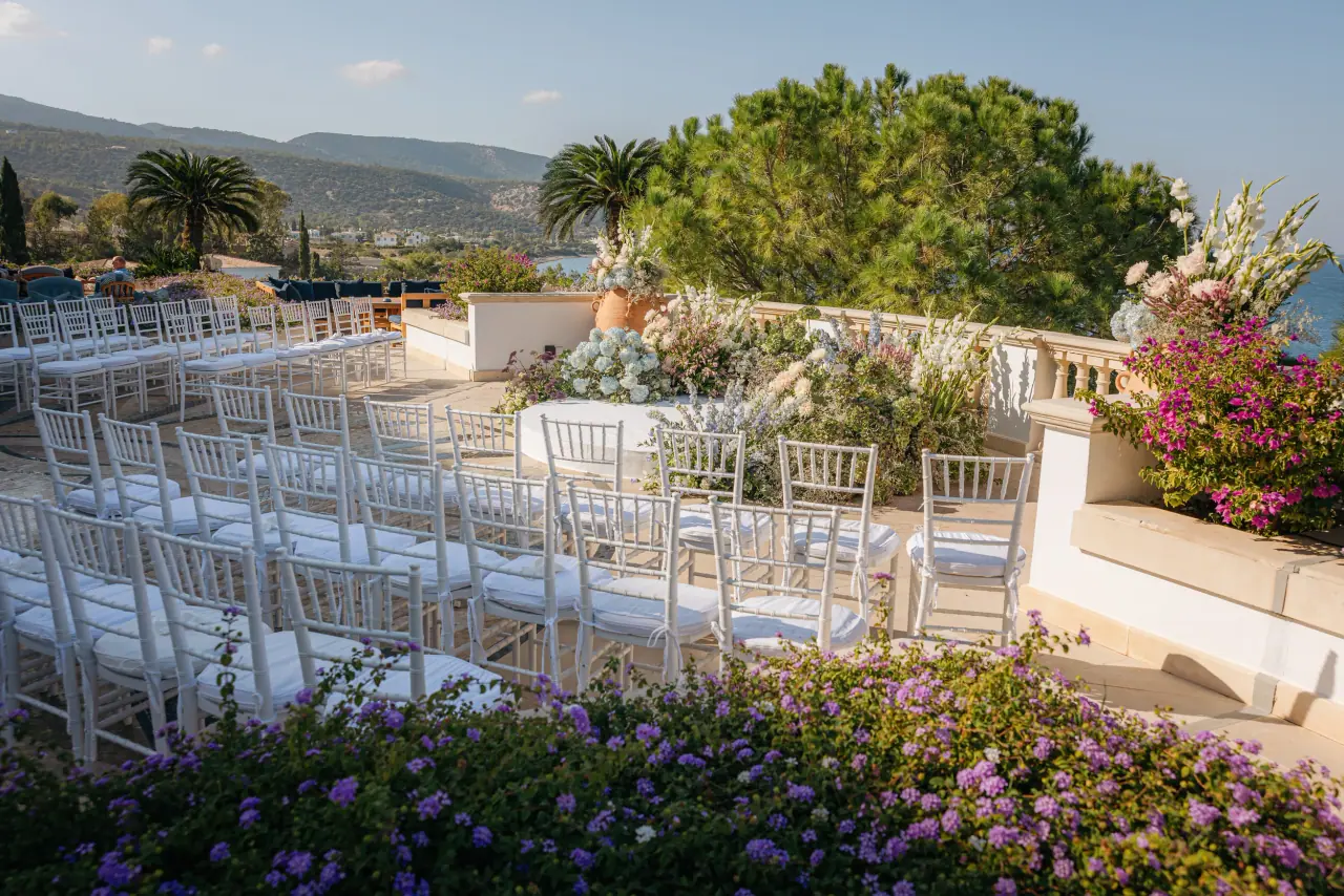 White chairs set on a flower-lined terrace overlooking the sea for a ceremony at Anassa